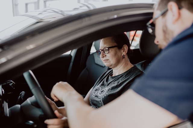Frau die in einem Auto sitzt und ein Mann der ihr etwas erklärt.