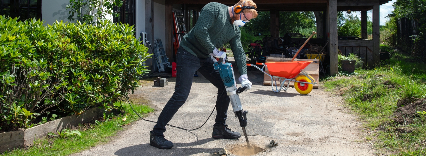 Mann mit Stemmhammer stemmt Auffahrt zum Einfamilienhaus auf.