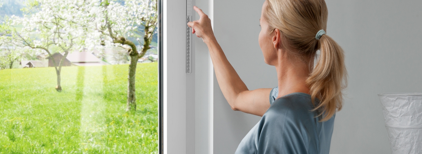 Eine Frau steht vor einem Fenster und deutet auf das Sonnenschutzsystem.