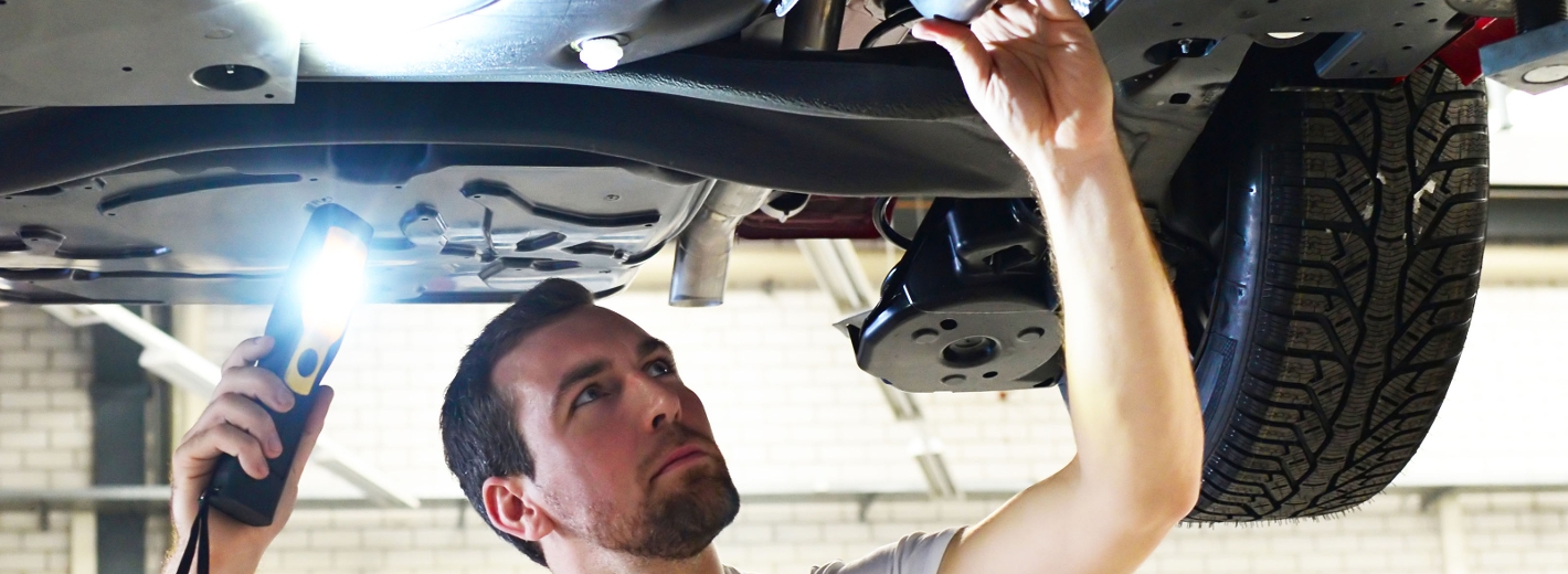 PKW Mechaniker kontrolliert den Unterboden eines Autos.