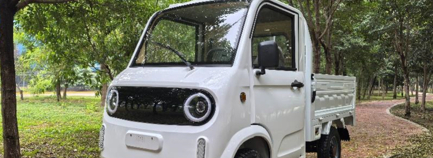 Eco-Rider Elektrolastenfahrzeug in der Farbe Weiß steht auf einem kleinen Weg in einem Park mit Bäumen.