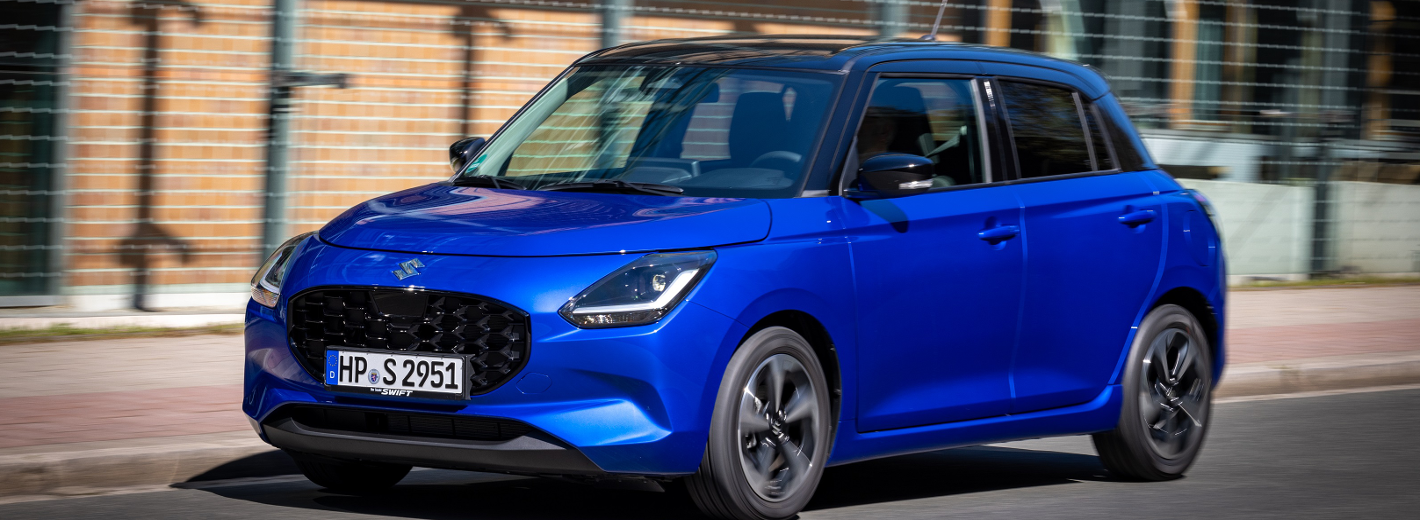 Blauer Suzuki Swift geparkt vor einem städtischen Basketballplatz.