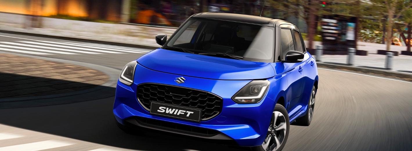 Suzuki Swift in Blau auf der Straße vor einem Zebrastreifen. Daneben das Logo der japanischen Auszeichnung RJC Car of the Year Award 2025