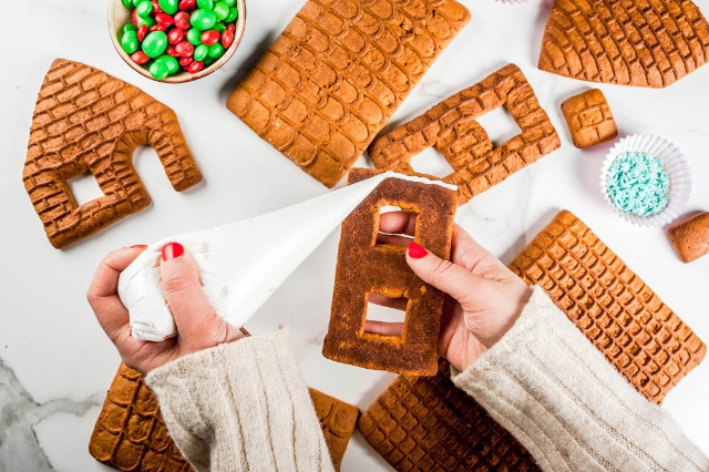 Hand drückt Zuckerguss auf Lebkuchenhausteil
