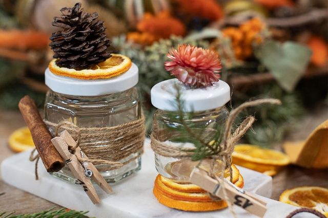 Zwei kleine Marmeladegläser dekoriert mit Zimtstange, Zapfen und getrockneter Blume und getrockneten Orangenscheiben