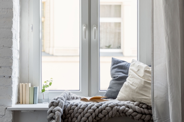Fensterbrett mit Pölster, einer gestrickten, grauen Decke und Bücher