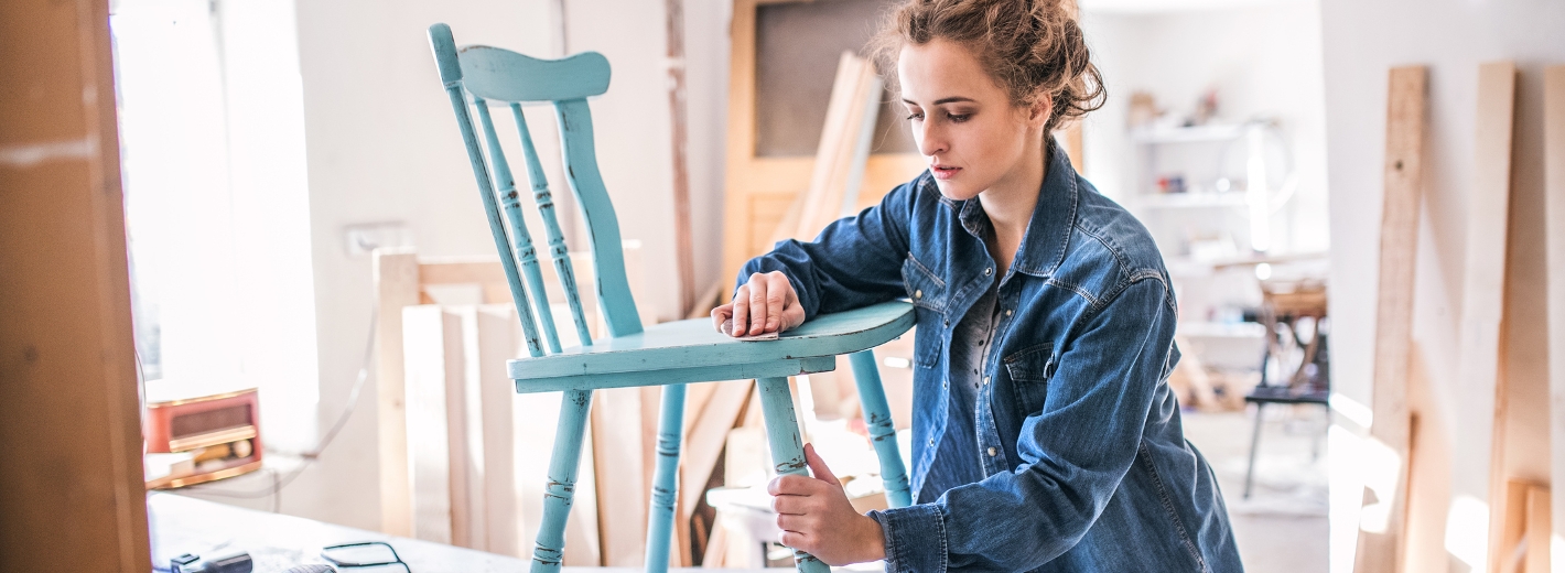 Frau schleift mit einem Schleifpapier einen blauen Stuhl aus Holz.