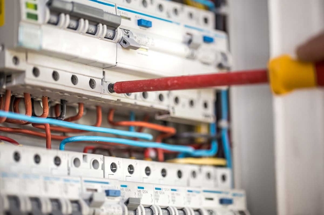 Elektriker, der mit seinem Schraubenzieher in einem Sicherheitskasten ist.
