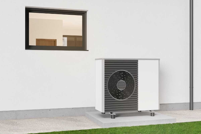 Eine moderne Wärmepumpe auf einem Podest im Garten eines neuen modernen Gebäudes.