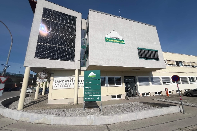 Auf dem Bild ist das Gasthaus zur Ähre in St. Pölten von Außen zu sehen. Ein graues Gebäude mit mehreren Photovoltaikpanelen und dem Lagerhaus-Logo mitten auf der Fassade. Vor dem Eingangsbereich steht eine Kreidetafel mit dem Tagesmenü, welches es zum Mittagessen gibt.