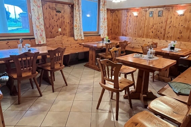 Auf dem Bild ist eine traditionelle Gaststube zu sehen die hauptsächlich aus Holz besteht. An den Fenstern sind mit einem Blumenmuster verzierten Vorhänge montiert.