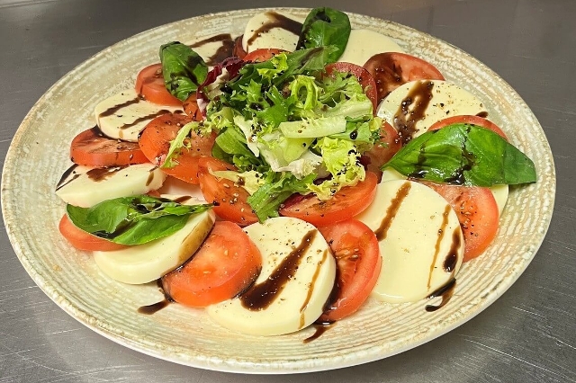 Auf dem Bild ist eine Portion eines frischen Mittagsmenüs des Lagerhaus Gasthauses zur Ähre zu sehen. Es handelt sich um Mozarella mit Tomaten, Basilikum und grünem Salat. Als Deko dient Acetto-Balsamico.
