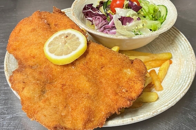 Ein golden gebratenes Schnitzel mit einem frischen, bunten Salat und krossen Pommes und einer Scheibe Zitrone.