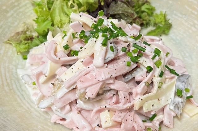Auf dem Bild ist ein schmackhafter Wurstsalat mit Käse zu sehen welcher mit grünem Salat und Schnittlauch dekoriert ist.