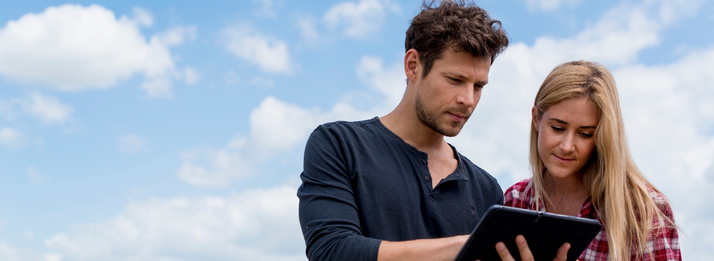 zwei Agrar Landwirte im Feld mit einigen Wolken am Himmel und einem Tablet in der Hand.