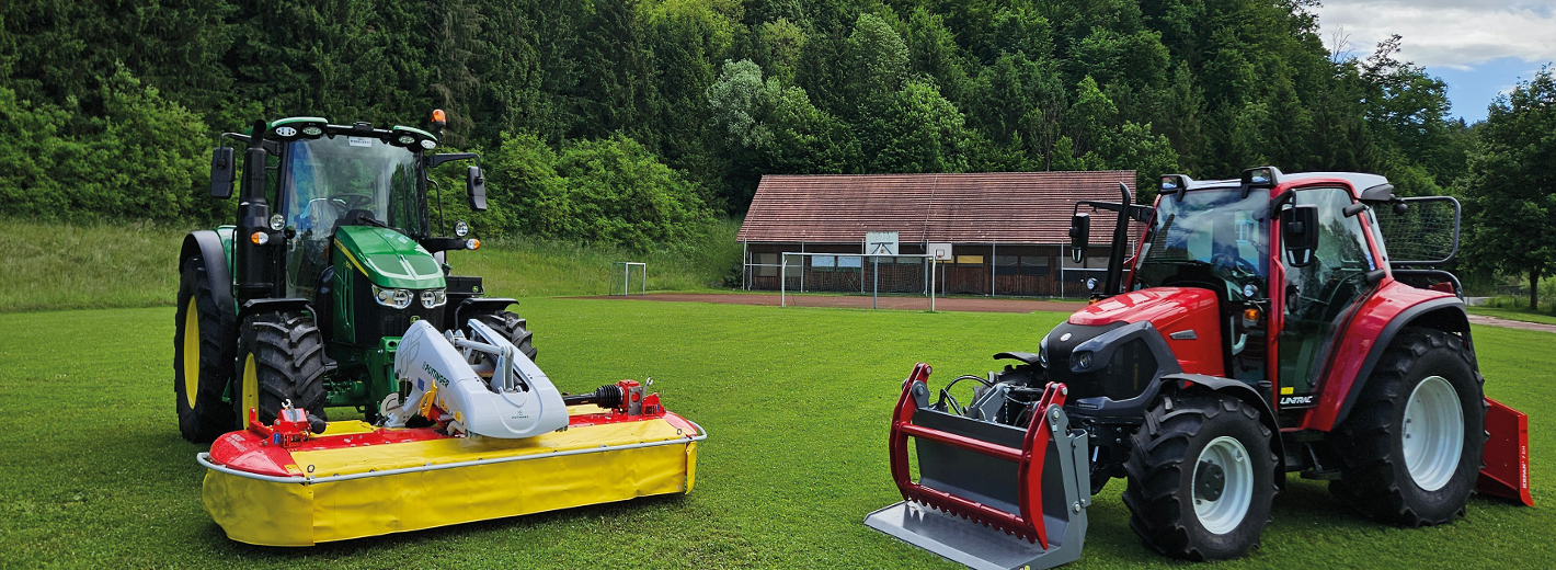 Ein John Deere und ein Lindner Traktor werden auf einer grünen Wiese präsentiert - im Hintergrund sieht man das Schloss Burgstall in Wies