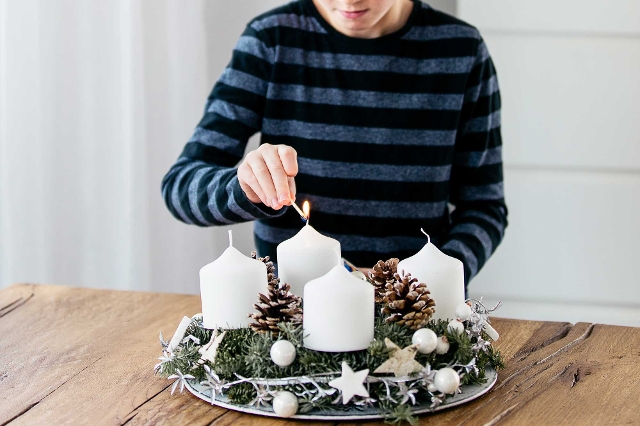 Adventkranz mit weißen Kerzen wird angezündet