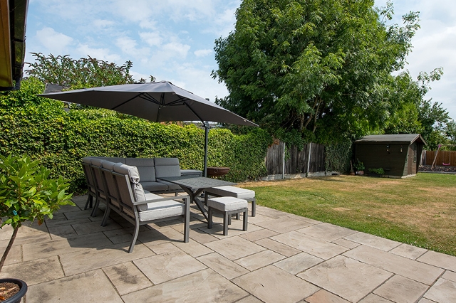 Terrasse mit Gartenmöbeln und Sonnenschirm neben gepflegtem Garten und Rasenfläche.