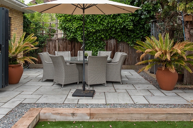 Terrasse mit Steinplatten, Gartenmöbeln und Sonnenschirm im gepflegten Garten.