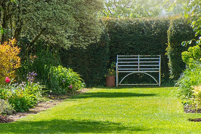 Gepflegter Garten mit grünem Rasen, Blumenbeeten und Sitzbank im Hintergrund.