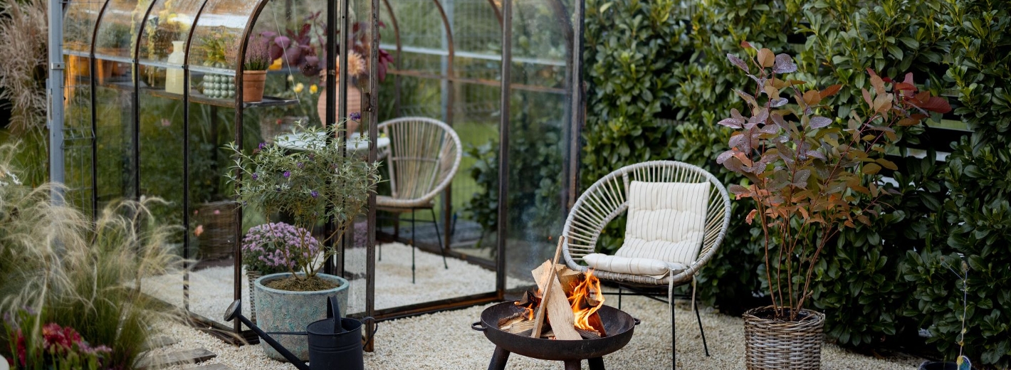Glashaus im Garten mit bepflanzten Regalen, Sitzgelegenheiten und Beleuchtung.