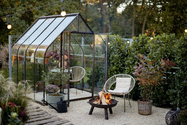 Glashaus im Garten mit bepflanzten Regalen, Sitzgelegenheiten und Beleuchtung.