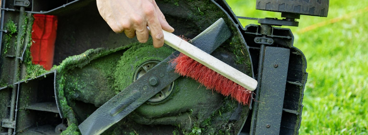 Mann reinigt Messer eines Rasenmähers mit einer Bürste