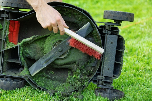 Mann reinigt Messer eines Rasenmähers mit einer Bürste