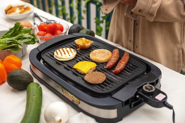 Elektrogrill auf einem Tisch mit Grillkäse, Gemüse und veganen Fleischalternativen