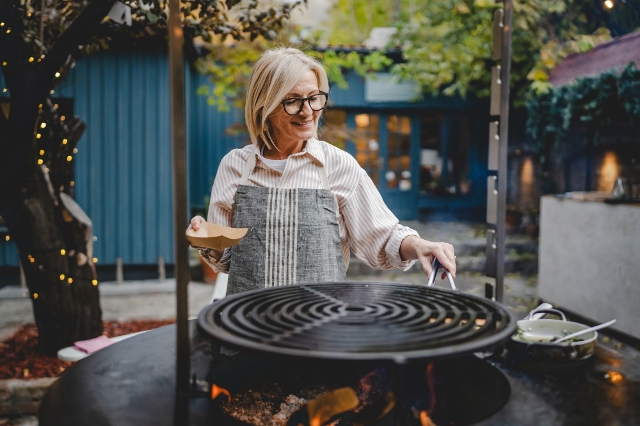 Frau legt Grillgut auf einer Feuerplatte – rustikales Kochen im Freien