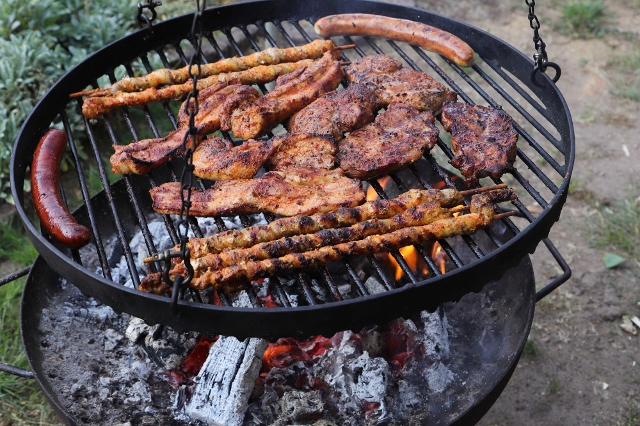 Fleisch und Würste brutzeln auf einem Grillaufsatz über einer Feuerschale
