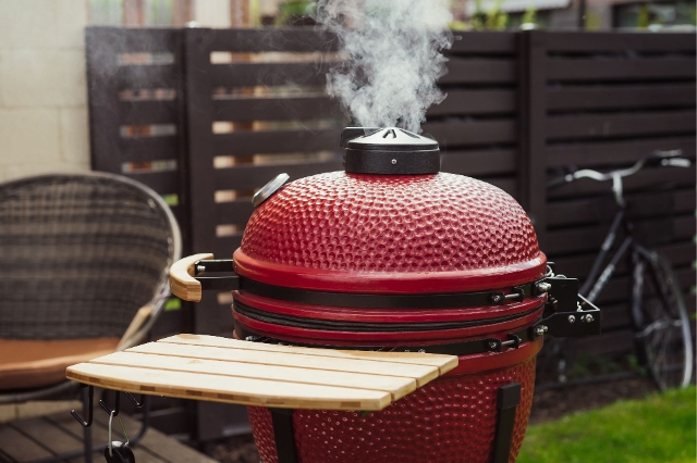 Rauch steigt aus einem roten Keramikgrill auf – intensive Hitze und Aroma beim Grillen
