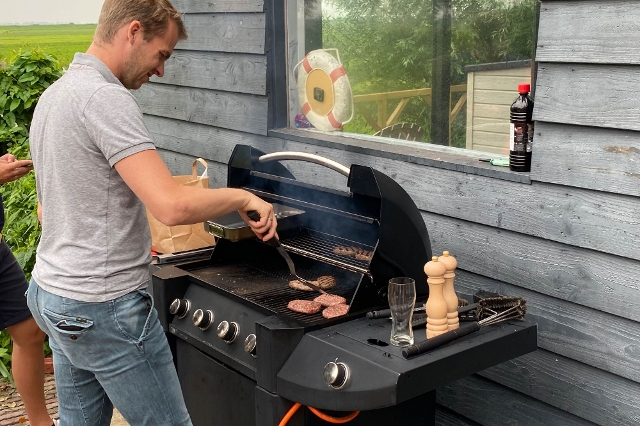 Mann grillt Burger Patties auf einem Gasgrill neben einer Holzhütte