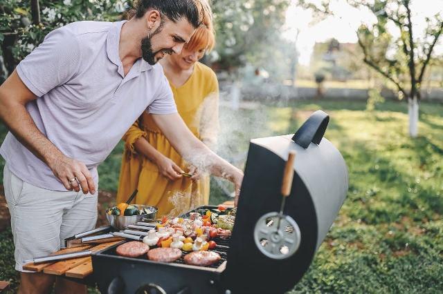 Junges paar legt Gemüsespieße und Faschiertes auf den Gartengriller auf