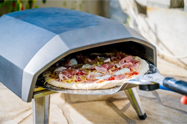 Gemüsepizza wird in einen mobilen Pizzaofen im Freien geschoben
