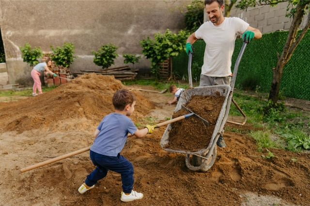 Vater mit Kindern beim Rasen anbauen mit Scheibtruhe und Erde.