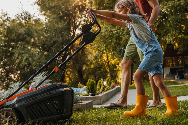 Kind hilft Vater beim Rasenmähen in frühabendlicher Sommerstimmung