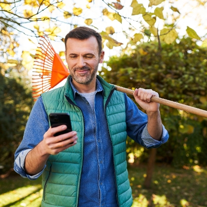 Mann, der einen Laubrechen und sein Handy in der Hand hält