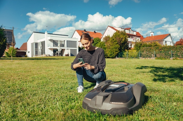 Smarter Rasenroboter am Mähen und einer jungen Frau am Handy