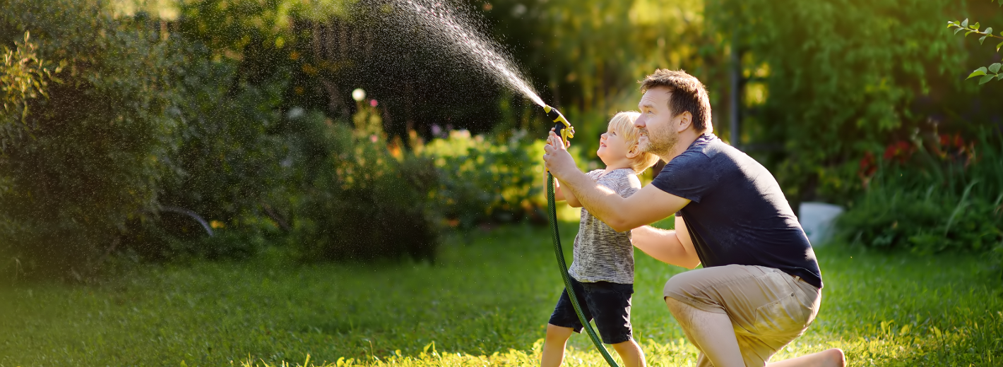 Vater und Sohn gießen mit dem Schlauch den Rasen