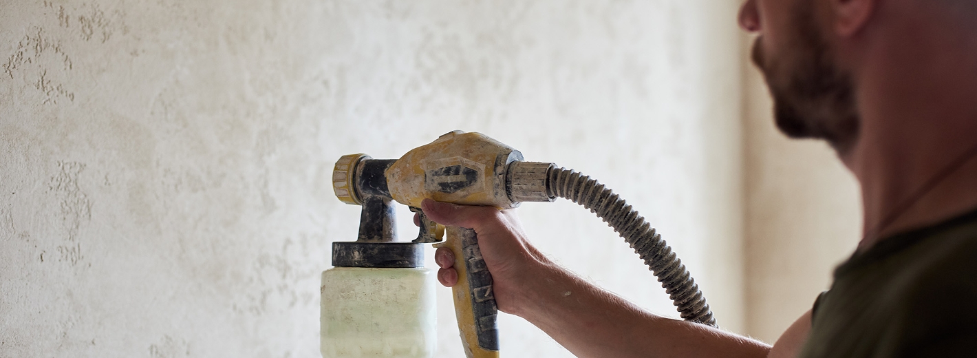 Mann grundiert Wand mit einem Sprühgerät