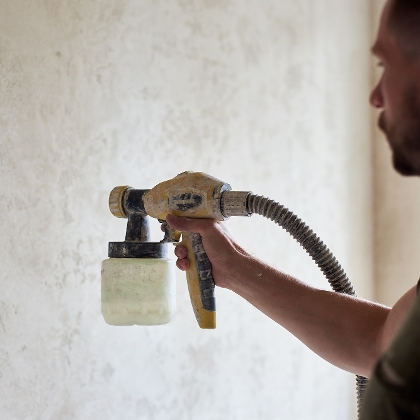 Mann grundiert Wand mit einem Sprühgerät