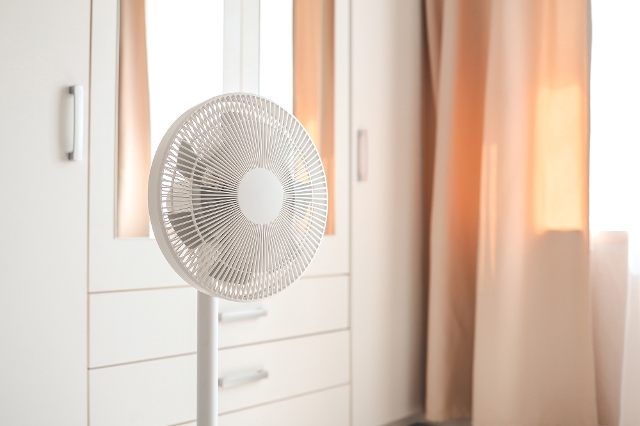 Standventilator steht im Schlafzimmer vor einem Vorhang.