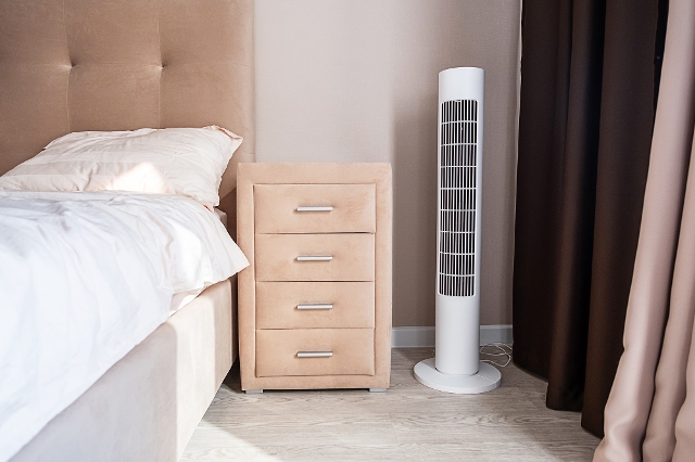 Modern eingerichtetes Schlafzimmer mit einem Turmventilator neben dem Bett.