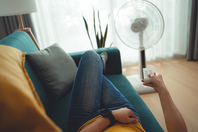 Frau liegt auf dem Sofa und steuert den Ventilator mit einer Fernbedienung.