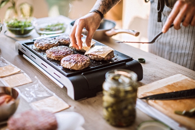 Mann grillt am Tischgrill Burger mit Käse