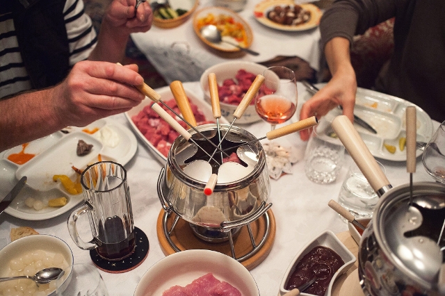 Gruppe isst gemeinsam Fondue mit Fleisch und Gemüse
