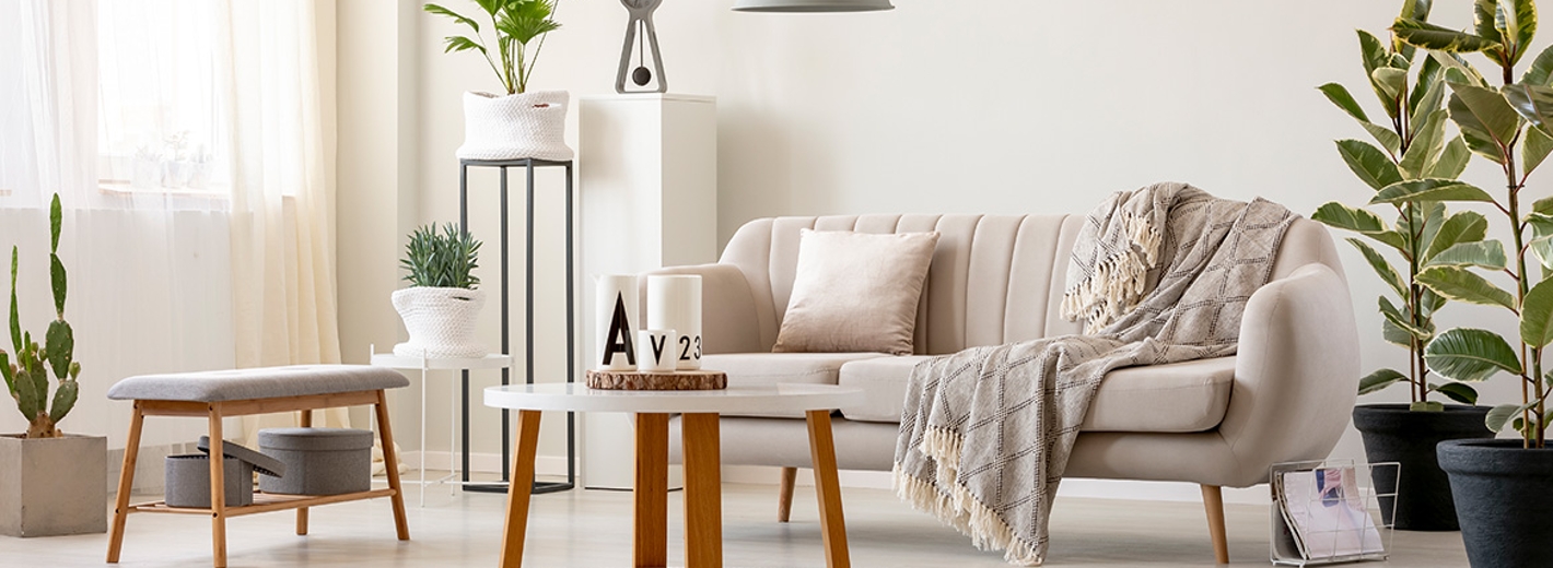Wohnzimmer in warmen weißen Farbtönen und grauen Akzenten, wie Lampe, Uhr und Hocker