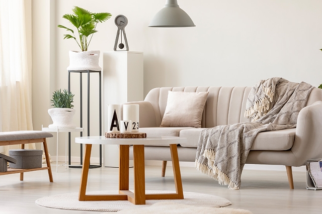 Wohnzimmer in warmen weißen Farbtönen und grauen Akzenten, wie Lampe, Uhr und Hocker
