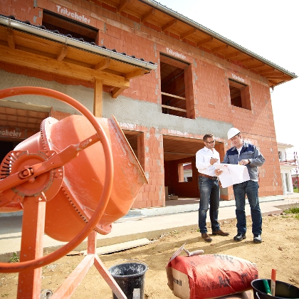 Baumeister und Bauherr mit Plan vor Rohbau